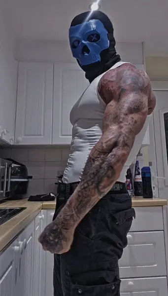 Zade, blue skull mask. Side profile in white vest, kitchen.