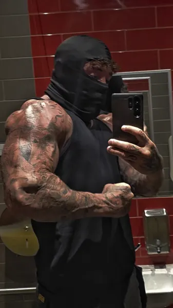 Zade, black balaclava. Mirror selfie in black vest, red-tiled gym washroom.