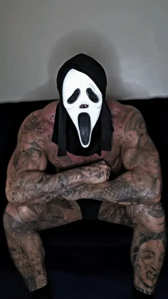 Zade, ghostface. Crouched, forearms on knees, dark backdrop.
