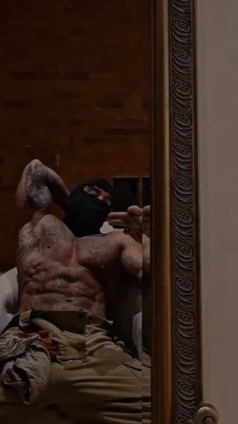 Zade, black balaclava. Reclining shirtless, reflected in a gilt mirror.