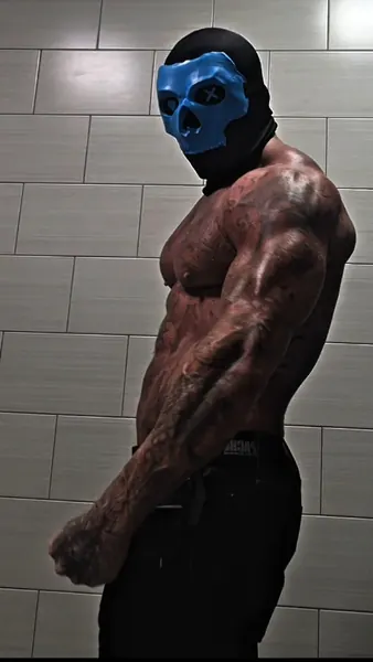 Zade, blue skull mask. Shirtless side profile, tiled wall.