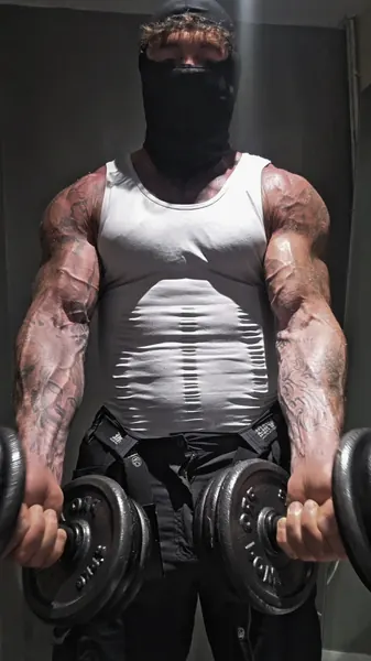 Zade, black balaclava. White vest, curling dumbbells.