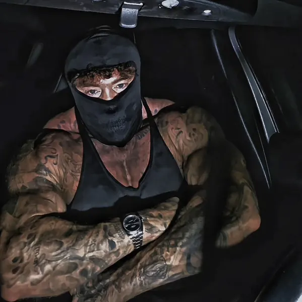 Zade, black balaclava. Moody close-up in dark car interior, black vest.