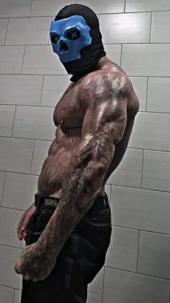 Zade, blue skull mask. Shirtless side profile, tiled wall.