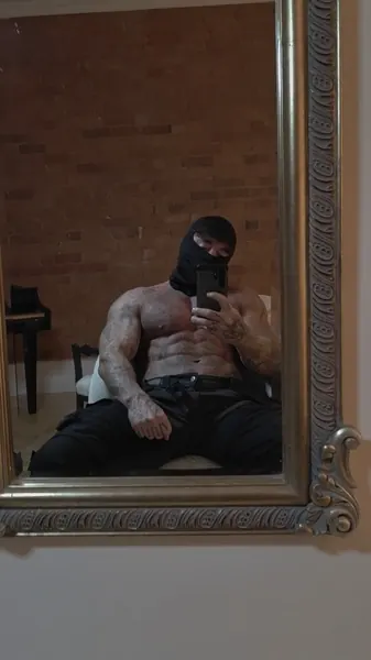 Zade, black balaclava. Seated shirtless, reflected in ornate mirror.