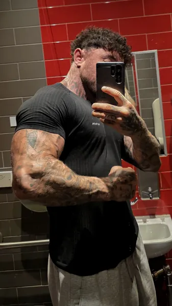 Zade, face hidden. Mirror selfie, phone over face, black tee, red tiles.